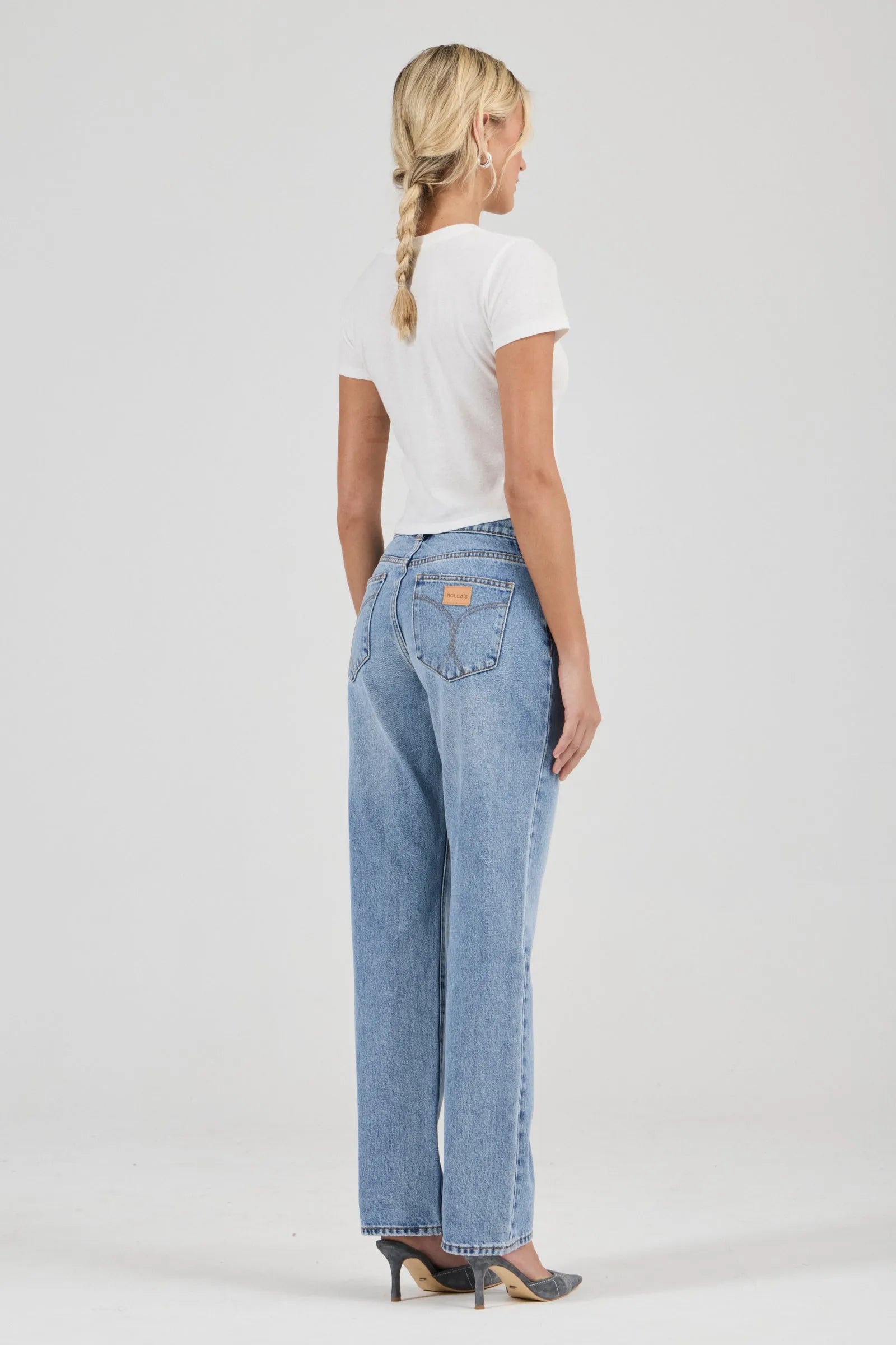 Woman wearing light blue jeans and a white t-shirt on a plain background