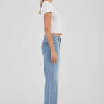Woman wearing light blue jeans and a white top on a plain background