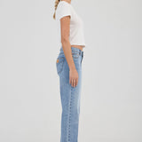 Woman wearing light blue jeans and a white top on a plain background