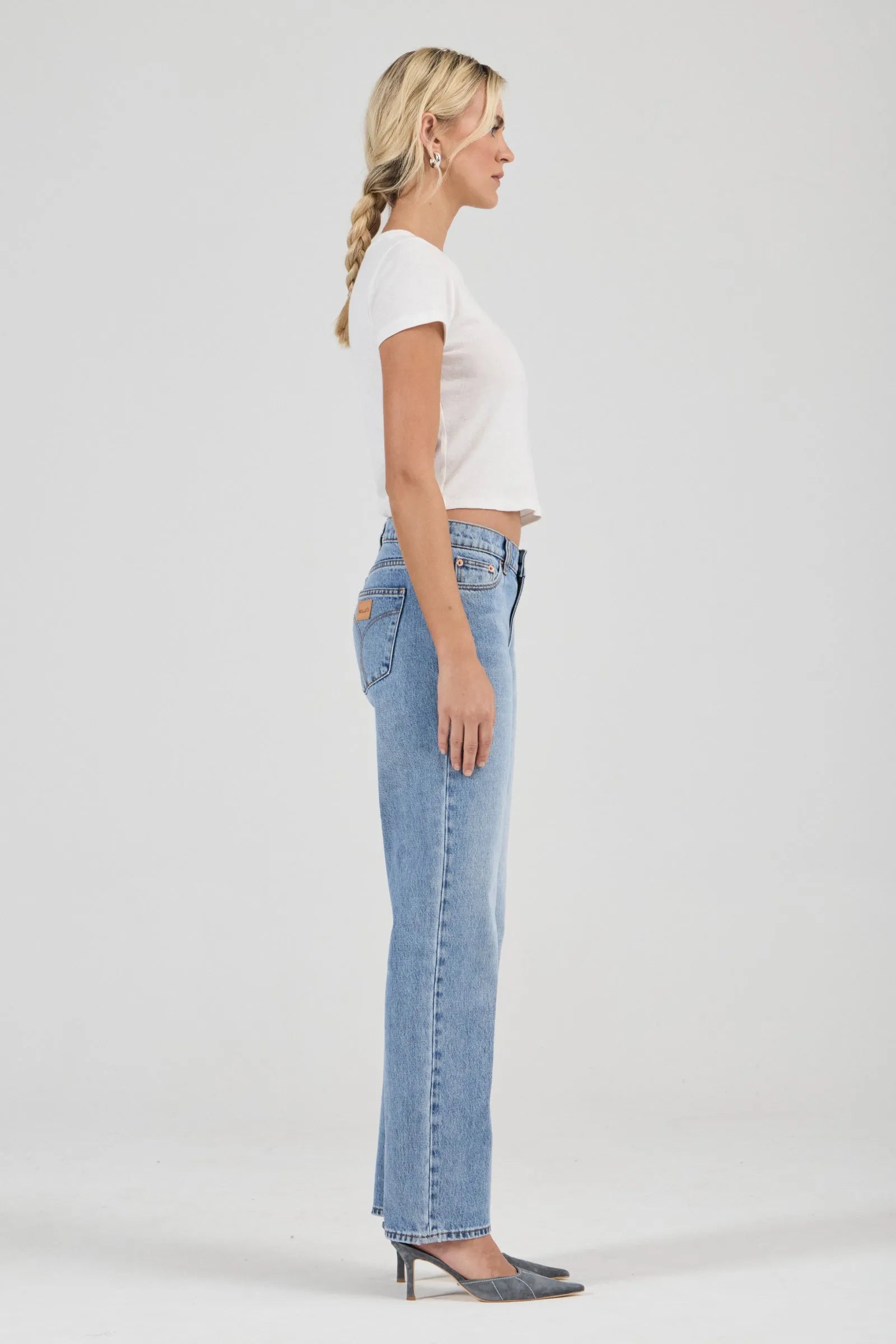 Woman wearing light blue jeans and a white top on a plain background
