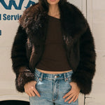 Woman wearing a fur coat and jeans standing in front of a white van with blue text.