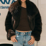 Woman wearing a fur coat and jeans standing in front of a white van with blue text.