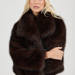 Woman wearing a dark brown fur coat against a plain background