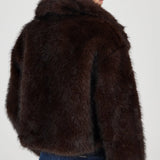 Person wearing a brown fur jacket on a plain background