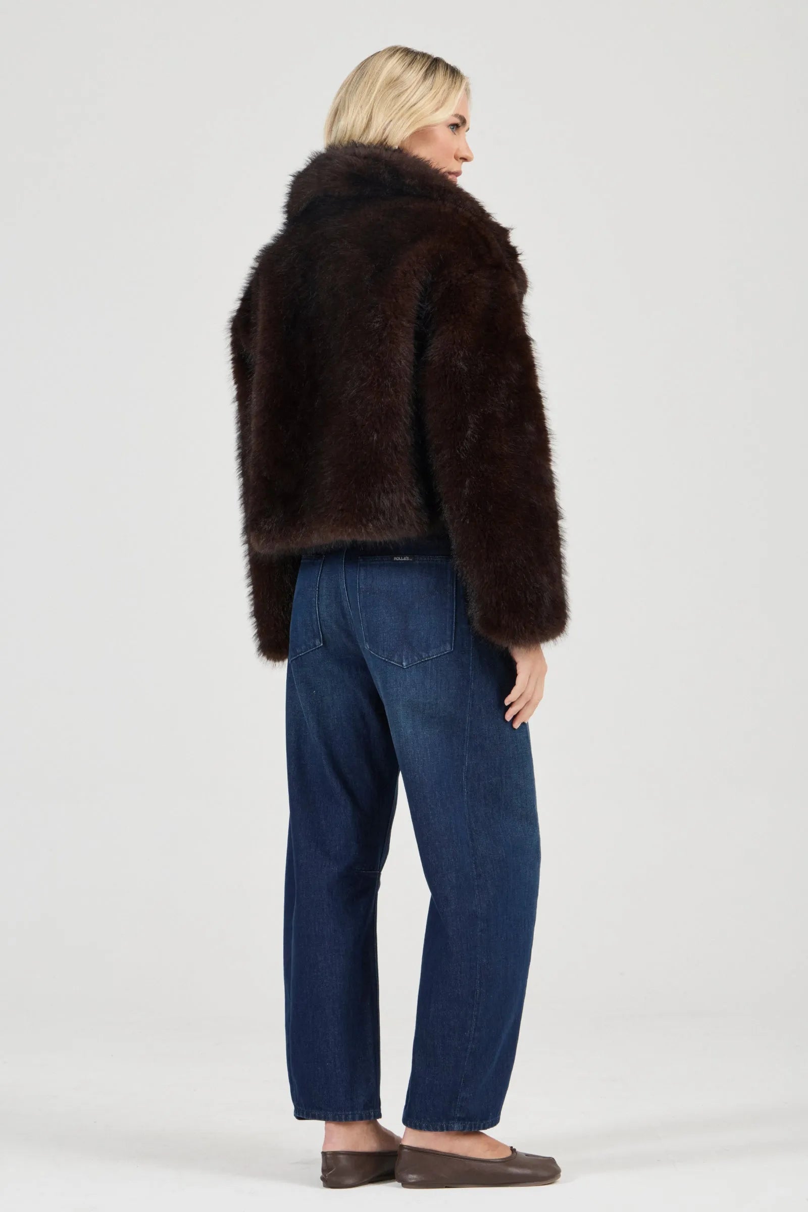 Woman wearing a brown fur coat and blue jeans on a white background