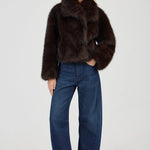 Woman wearing a brown fur coat and blue jeans on a white background