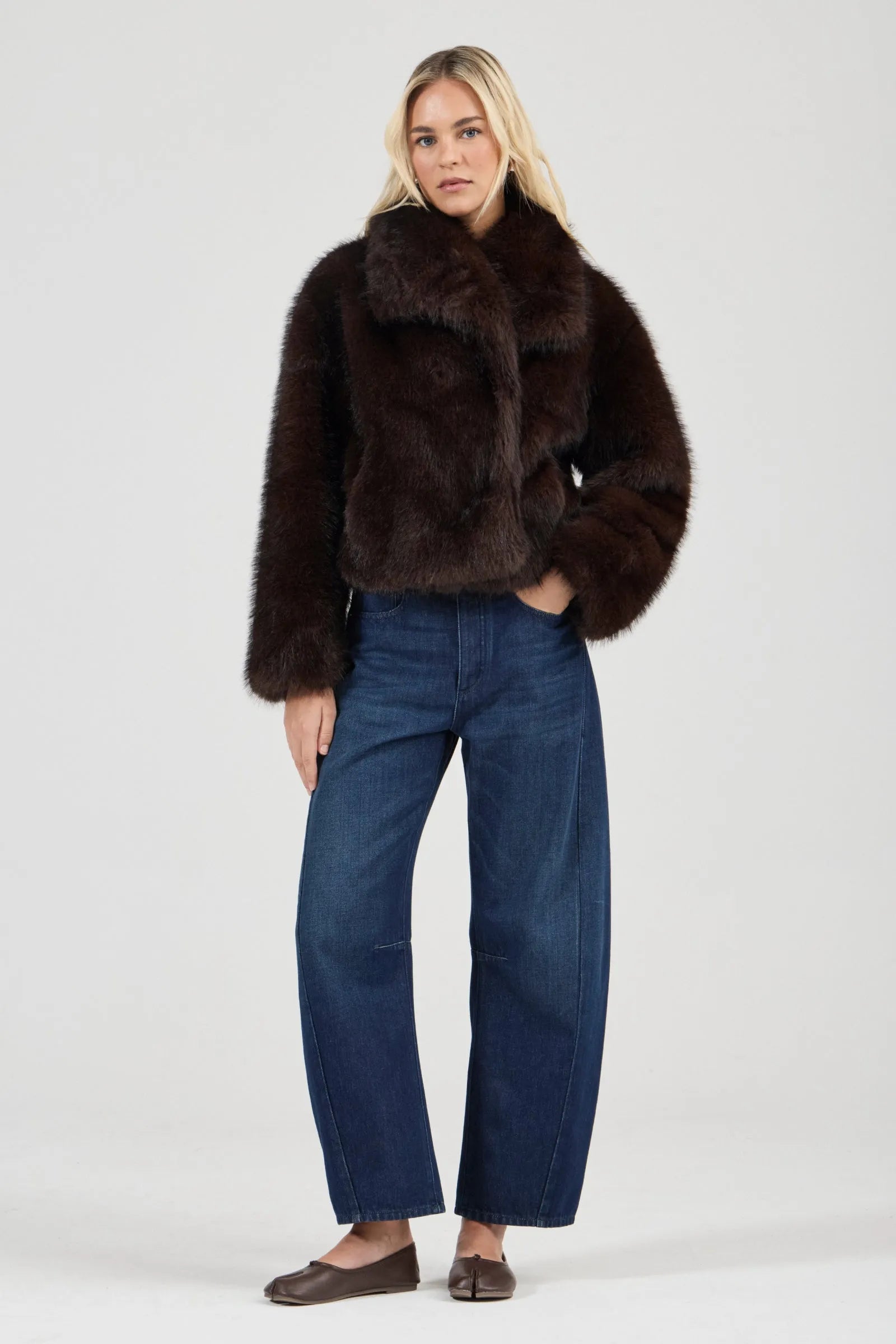Woman wearing a brown fur coat and blue jeans on a white background