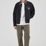Person wearing a dark jacket, white shirt, and brown pants on a white background