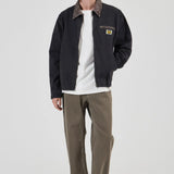 Person wearing a dark jacket, white shirt, and brown pants on a white background