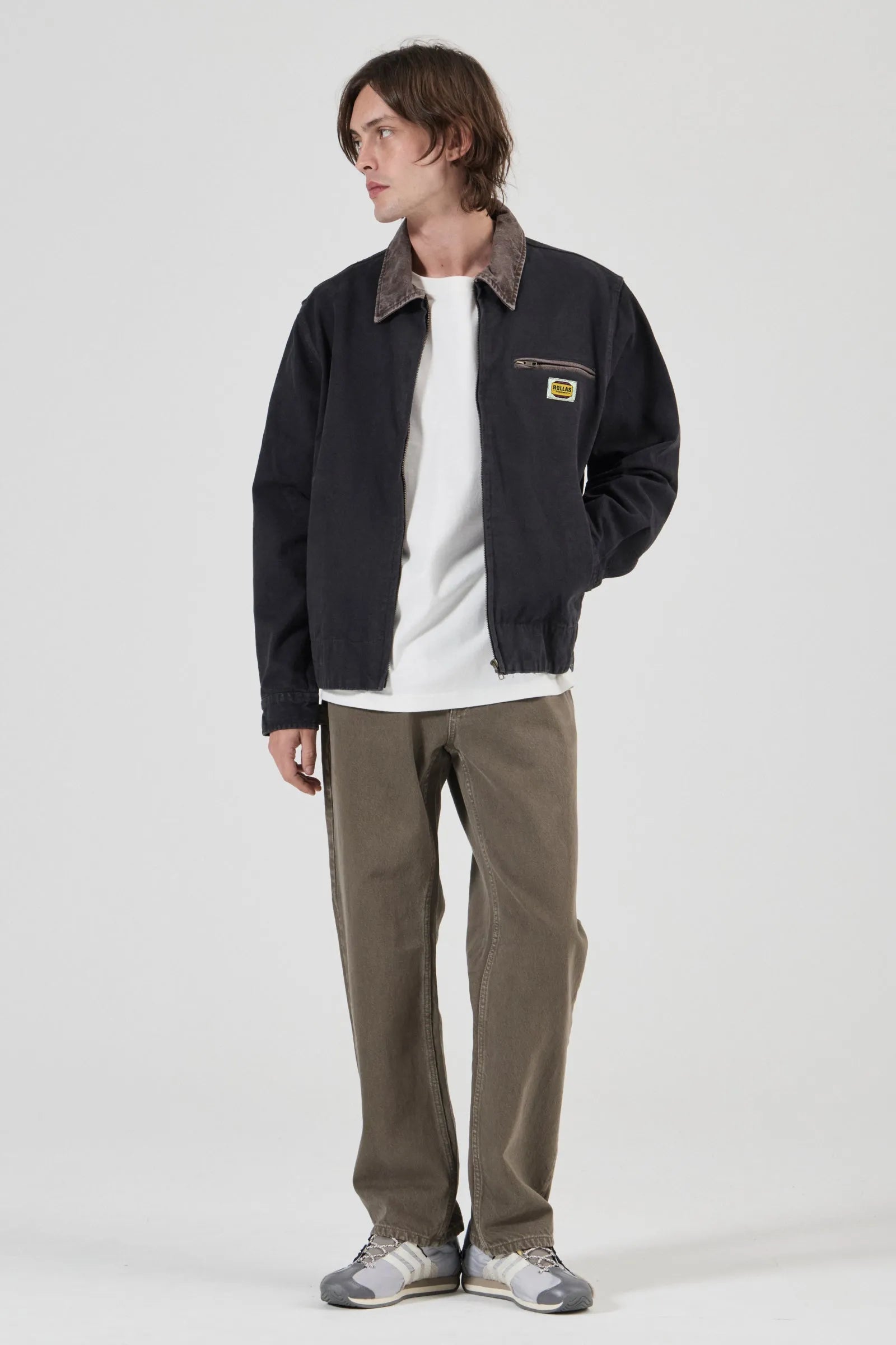 Person wearing a dark jacket, white shirt, and brown pants on a white background