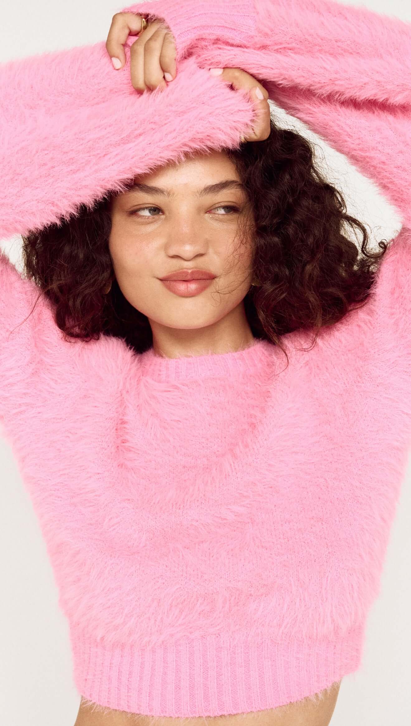 Person wearing a pink fuzzy sweater with a white background