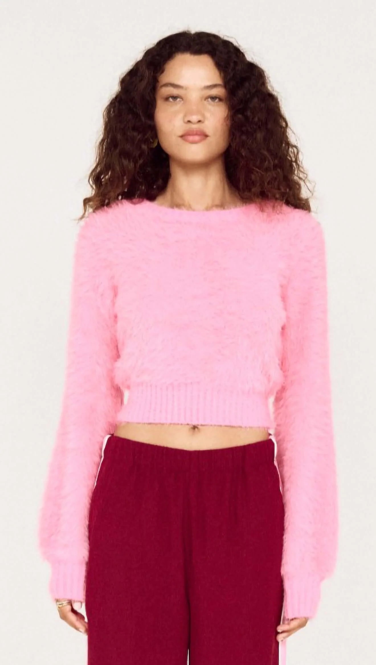 Person wearing a pink sweater and burgundy pants on a white background