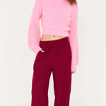 Woman wearing a pink sweater and burgundy pants on a white background