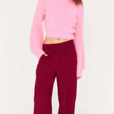 Woman wearing a pink sweater and burgundy pants on a white background