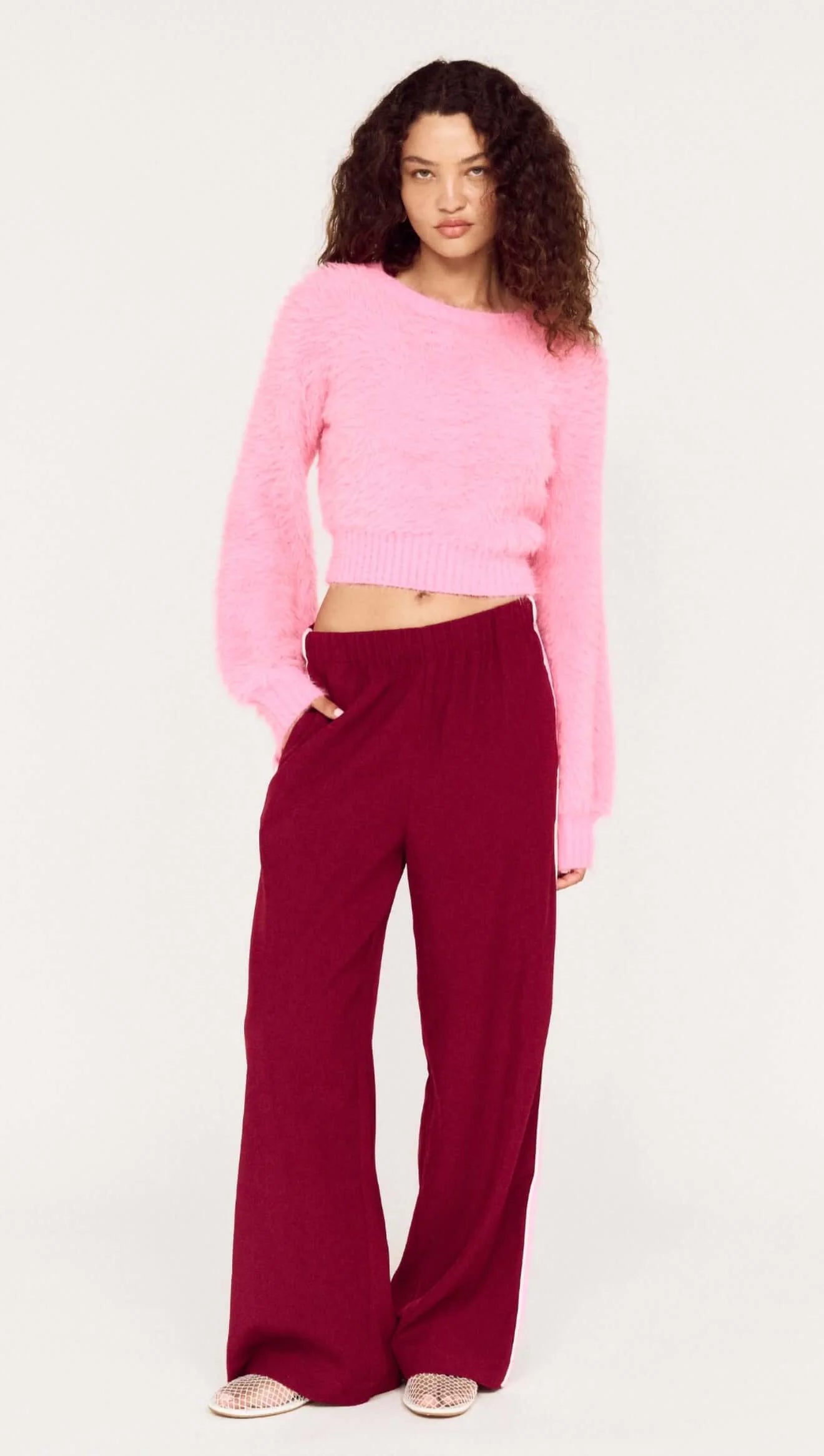 Woman wearing a pink sweater and burgundy pants on a white background