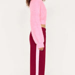 Person wearing a pink sweater and burgundy pants with white stripes on a white background