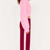 Person wearing a pink sweater and burgundy pants with white stripes on a white background