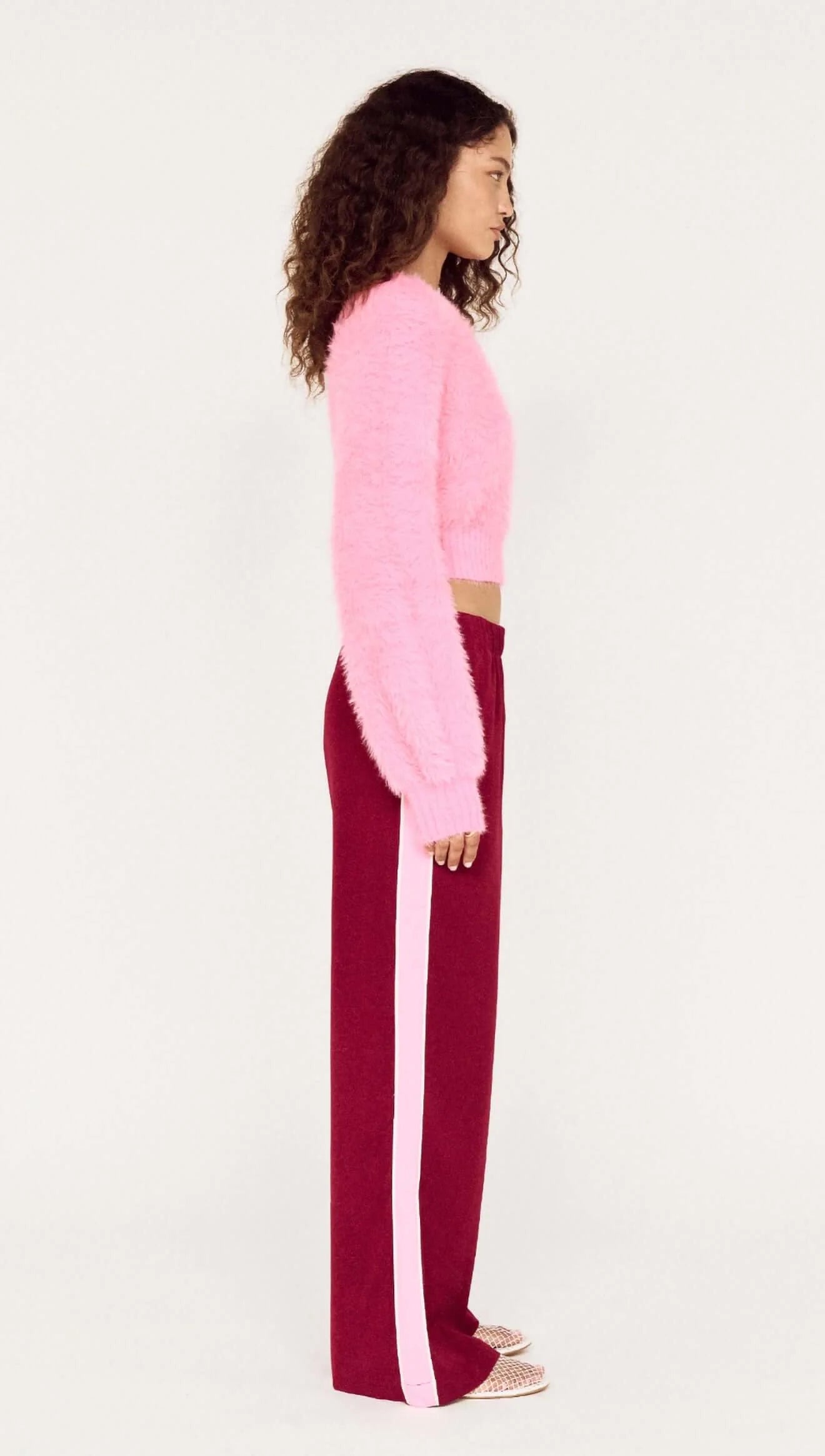 Person wearing a pink sweater and burgundy pants with white stripes on a white background