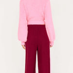 Person wearing a pink sweater and burgundy pants on a white background