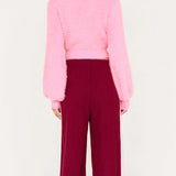 Person wearing a pink sweater and burgundy pants on a white background
