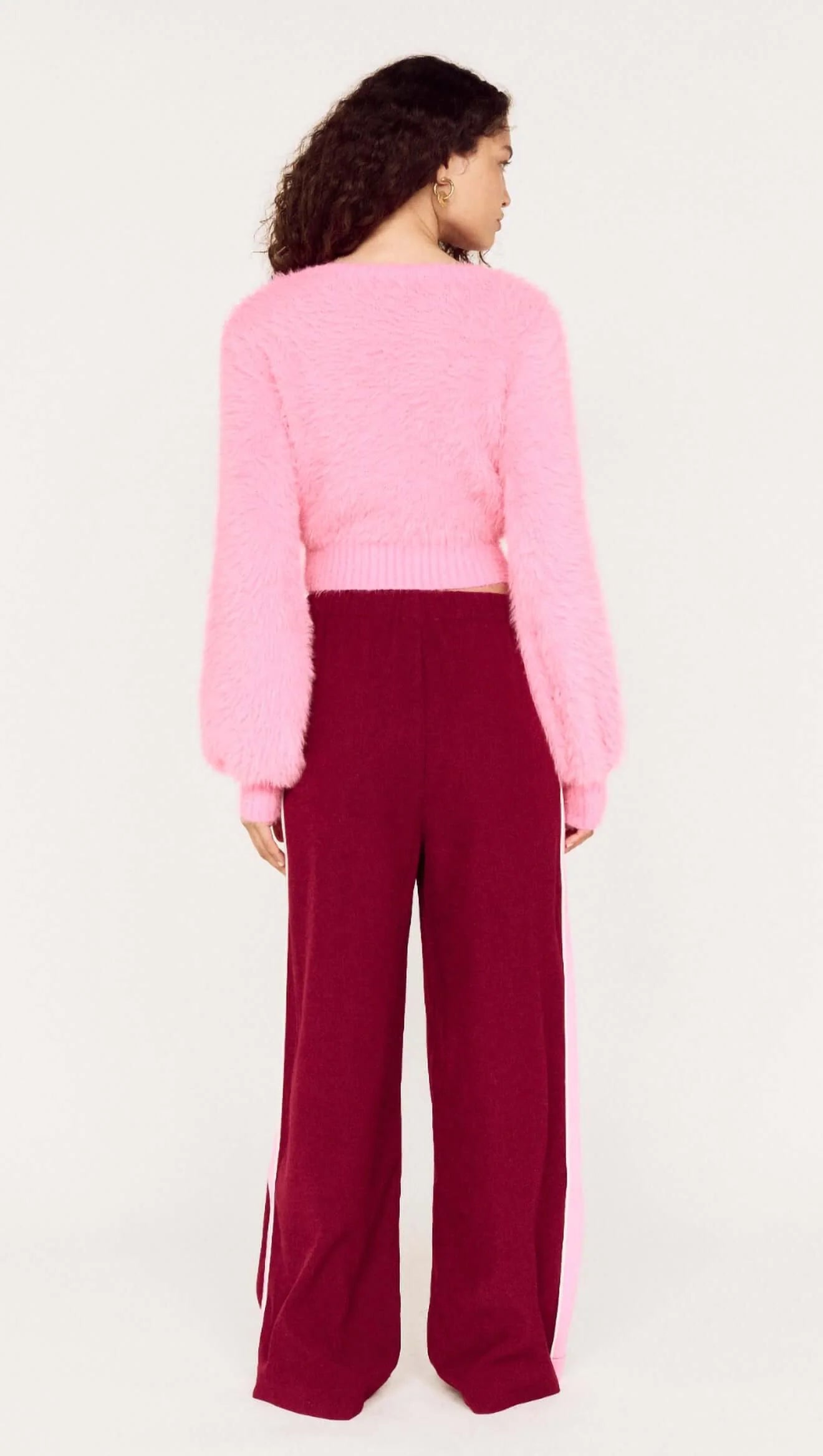 Person wearing a pink sweater and burgundy pants on a white background