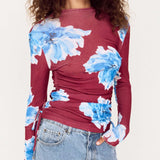 Woman wearing a burgundy long-sleeve top with blue floral patterns and light blue jeans.