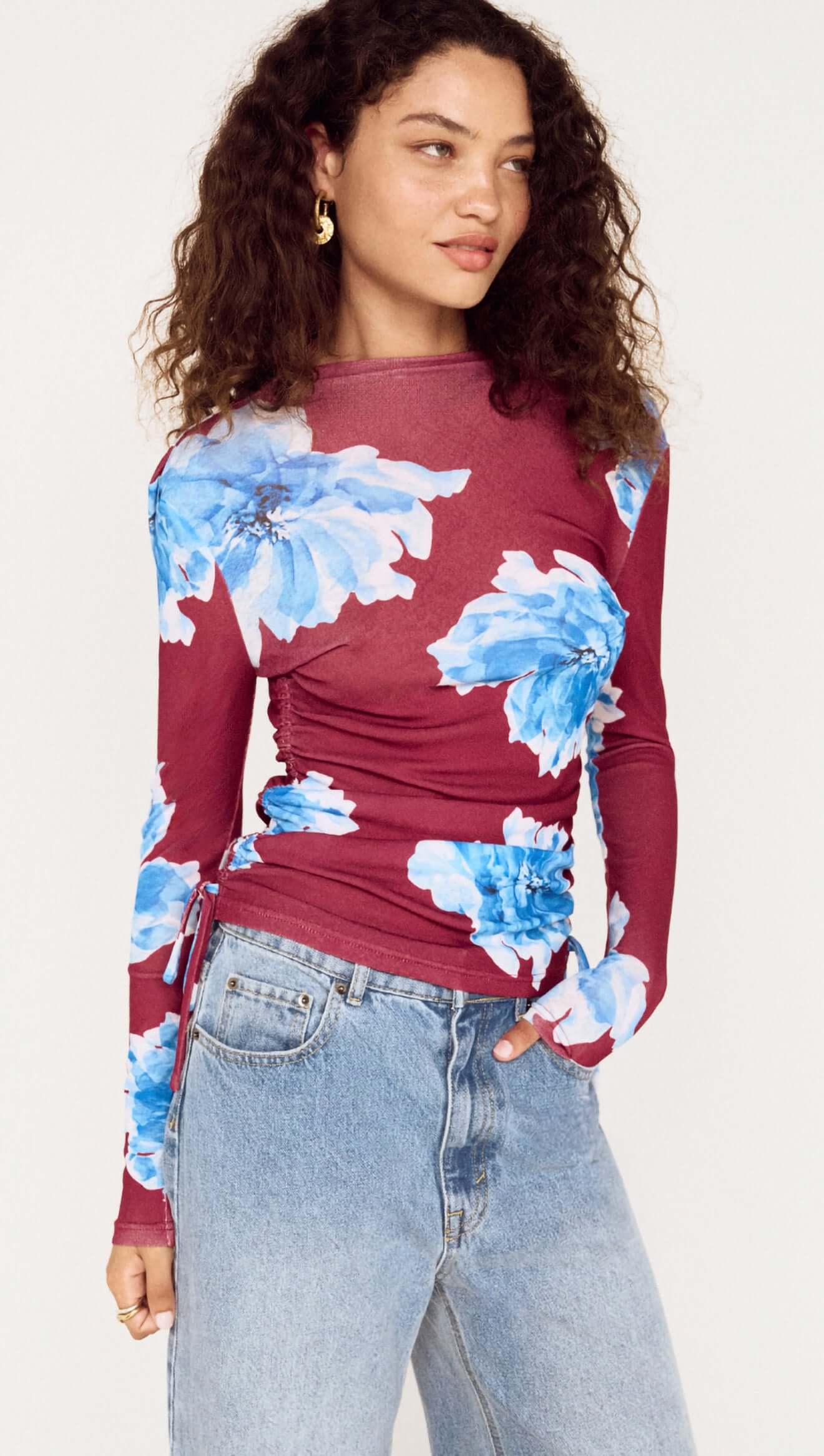 Woman wearing a burgundy long-sleeve top with blue floral patterns and light blue jeans.