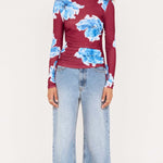 Woman wearing a burgundy sweater with blue floral patterns and light blue jeans on a white background