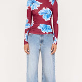 Woman wearing a burgundy sweater with blue floral patterns and light blue jeans on a white background