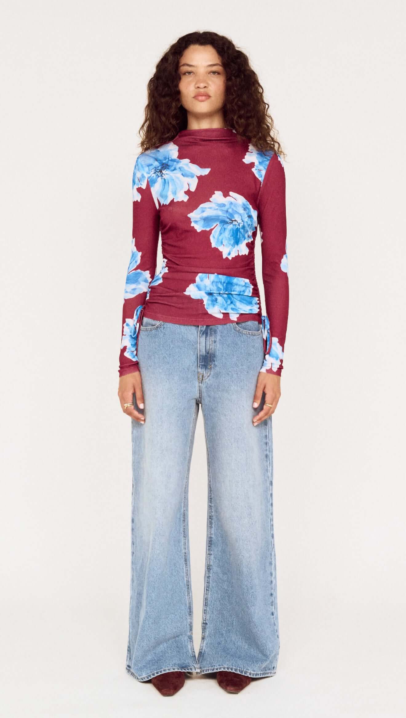 Woman wearing a burgundy sweater with blue floral patterns and light blue jeans on a white background