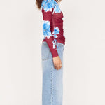 Person wearing a red and blue floral jacket with light blue jeans on a white background