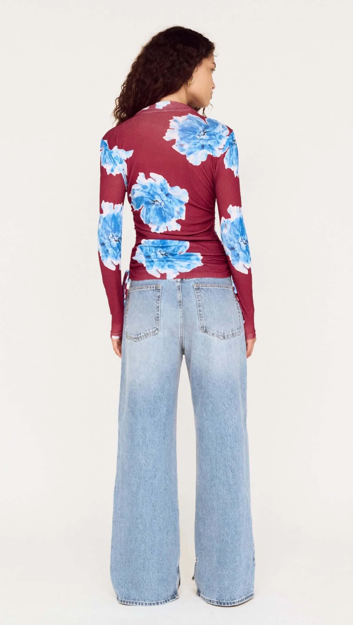 Person wearing a red floral top and light blue jeans on a white background