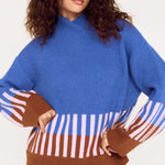 Woman wearing a blue sweater with brown and white striped sleeves on a white background