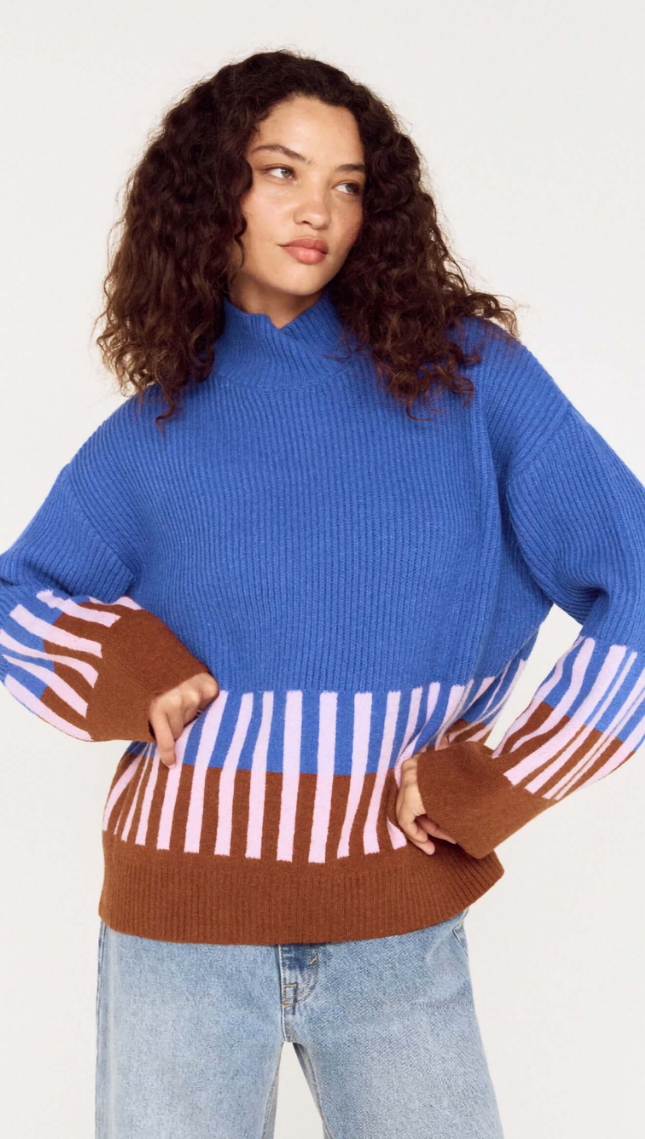 Woman wearing a blue sweater with brown and white striped sleeves on a white background