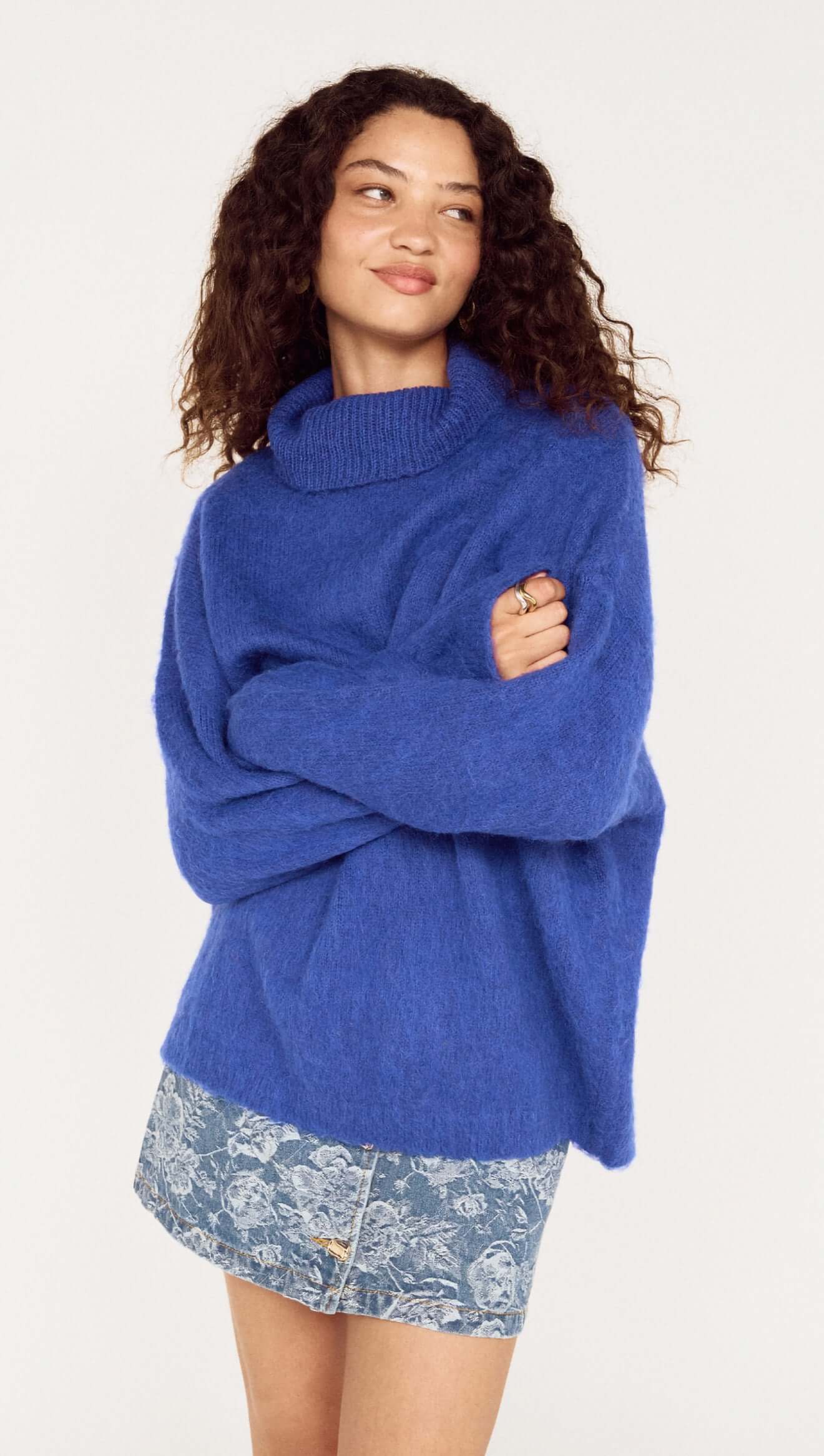 Woman wearing a blue sweater over a floral dress on a white background