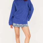 Woman wearing a blue sweater and patterned shorts on a white background