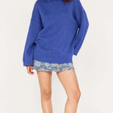 Woman wearing a blue sweater and patterned shorts on a white background