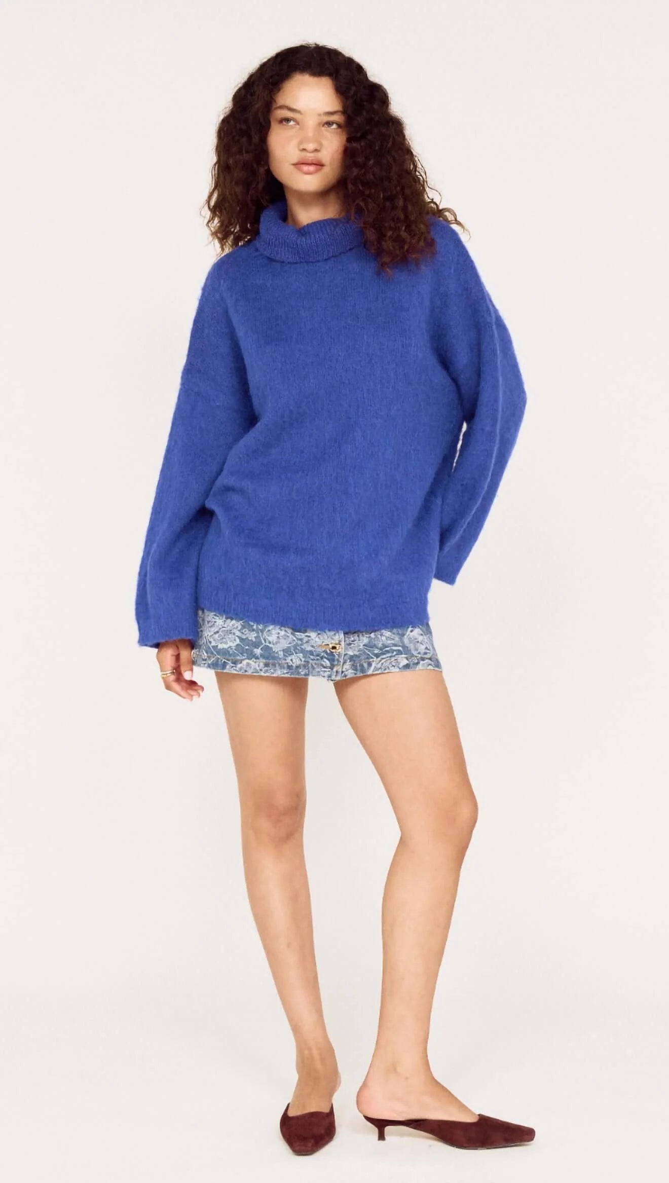 Woman wearing a blue sweater and patterned shorts on a white background