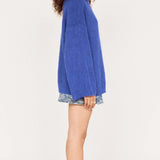 Woman wearing a blue sweater and patterned shorts on a white background