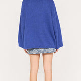 Person wearing a blue sweater and floral shorts on a white background