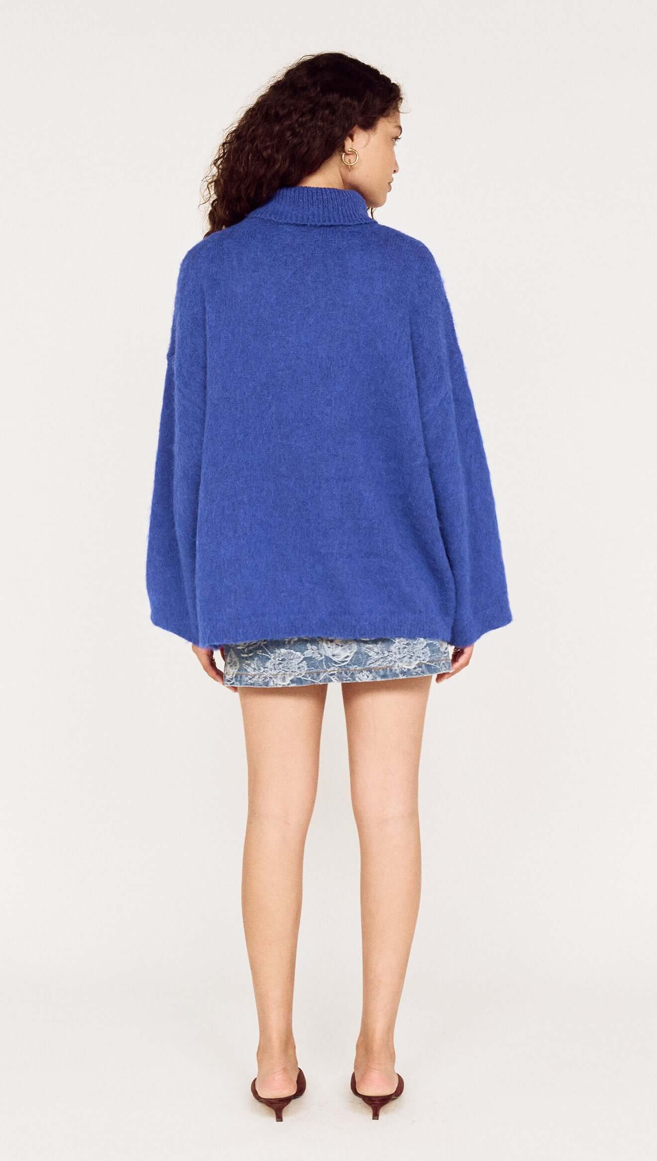 Person wearing a blue sweater and floral shorts on a white background