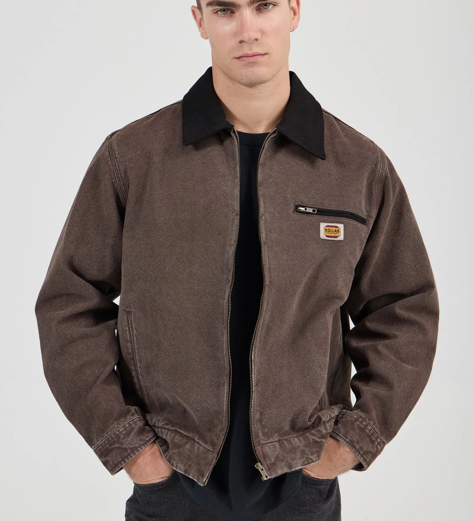 Man wearing a brown jacket with a visible brand logo on a white background