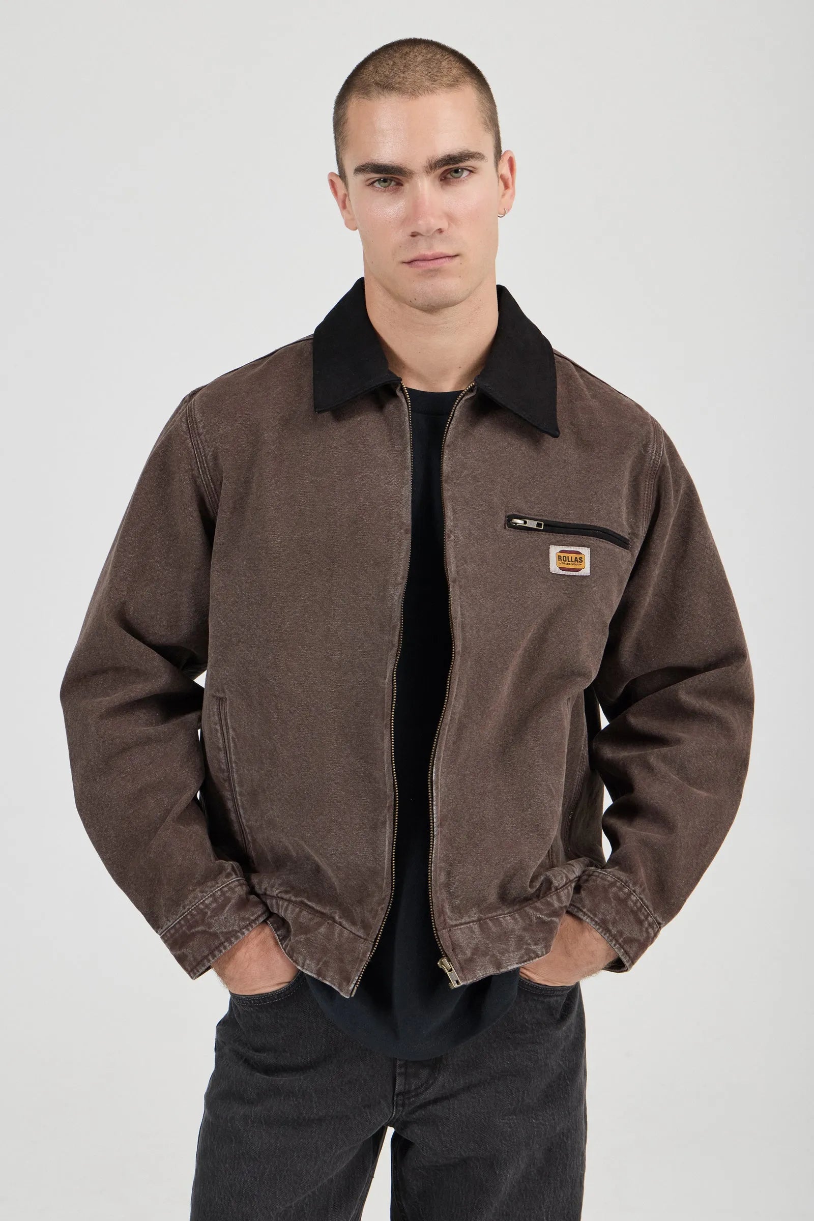 Man wearing a brown jacket with a visible brand logo on a white background