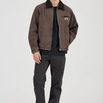 Man wearing a brown jacket and dark pants on a white background