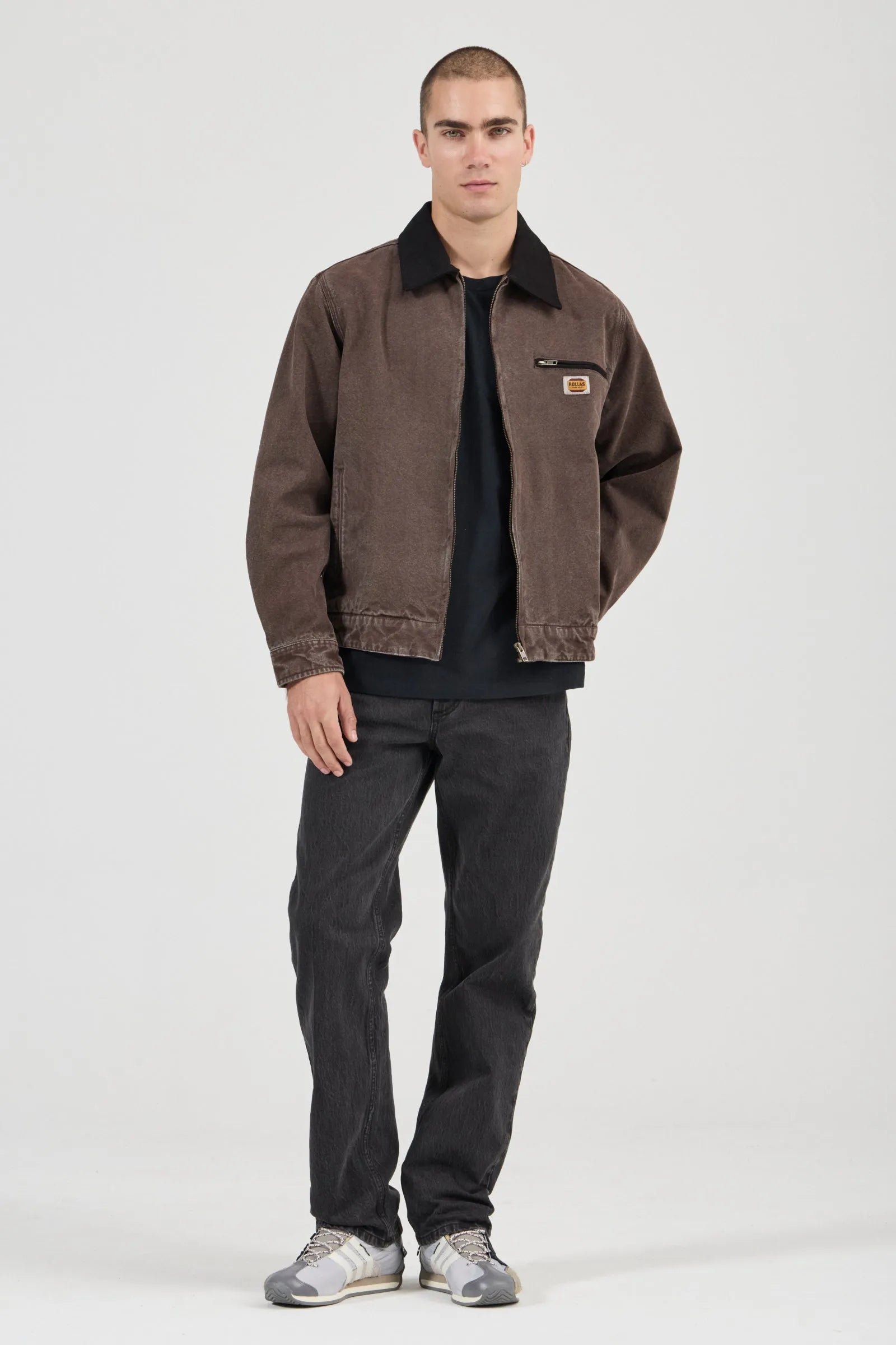 Man wearing a brown jacket and dark pants on a white background