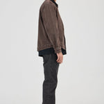 Man wearing a brown jacket and dark jeans standing against a white background