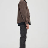 Man wearing a brown jacket and dark jeans standing against a white background