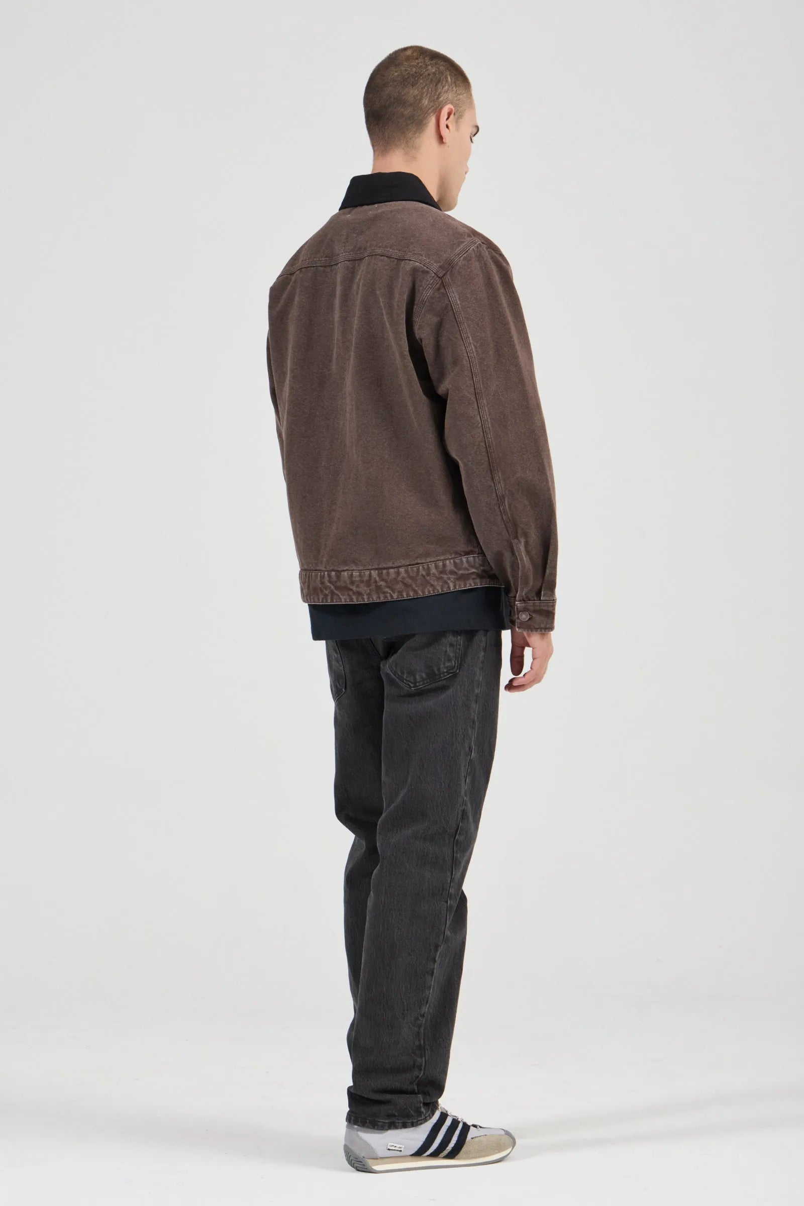 Man wearing a brown jacket and dark jeans on a white background