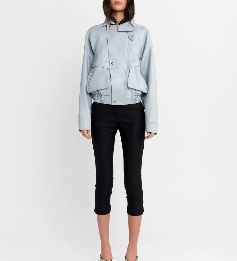 A model stands against a plain white studio background wearing a light blue cropped jacket, black cropped pants, and black-and-white striped high-heeled sandals.