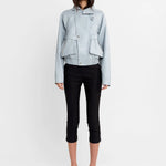 A model stands against a plain white studio background wearing a light blue cropped jacket, black cropped pants, and black-and-white striped high-heeled sandals.